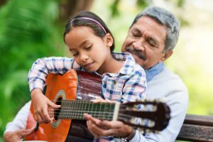 Cropped shot of an adorable little girl learning how to play the guitar while enjoying the day outdoors with her granddad